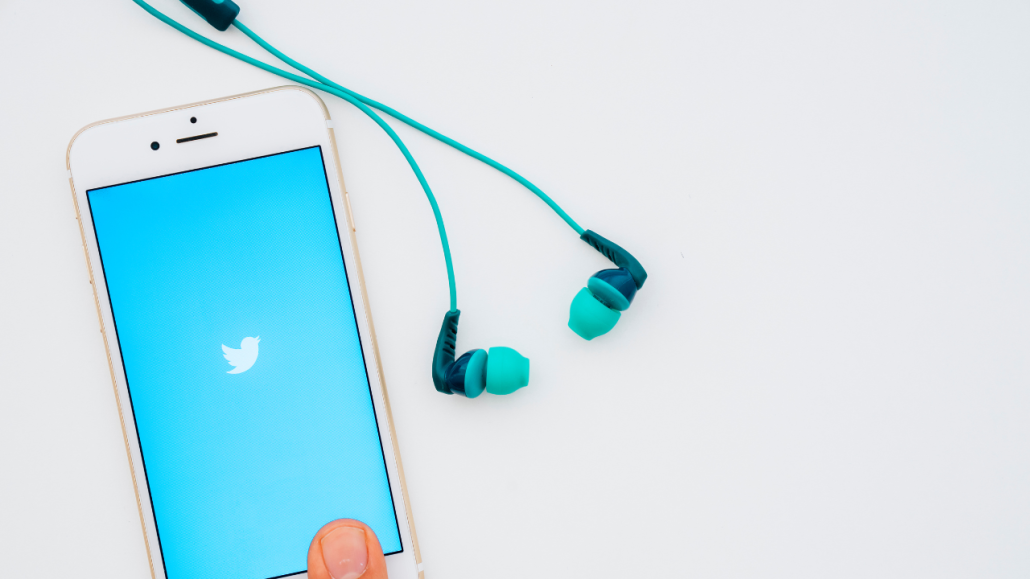 Mobiltelefon med Twitter-logga pÄ skÀrmen. Och ett par hörlurar intill.